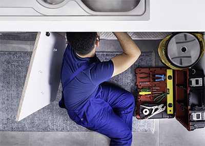 Ariel photo of a plumber working on plumbing under the kitchen sink