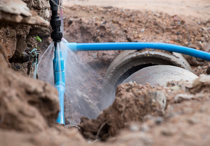 broken blue sewer line with water spraying out