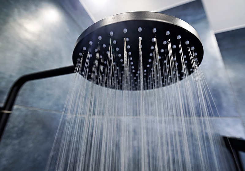 closeup of a silver shower head spraying fine lines of water in a black tiled shower